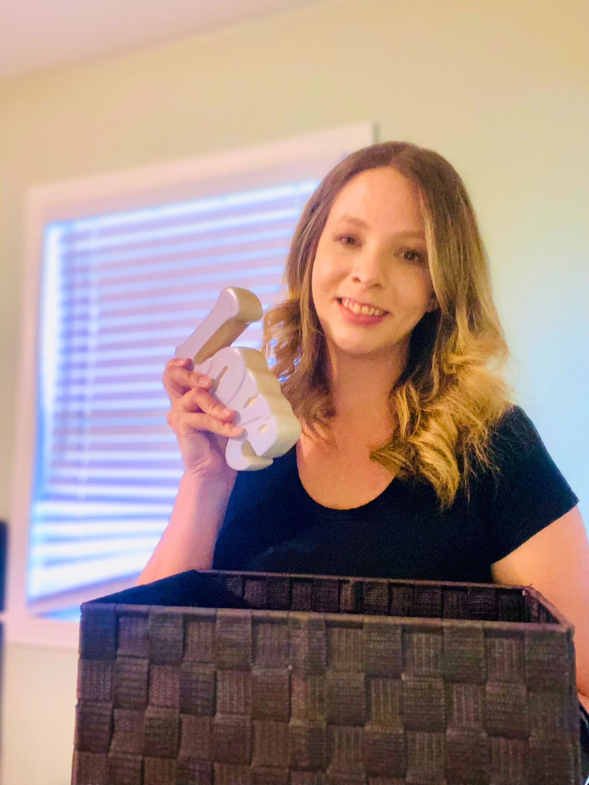 Smiling mom holding white organizers while decluttering a basket in a bright, cozy room — demonstrating simple, no mess decluttering for busy moms.